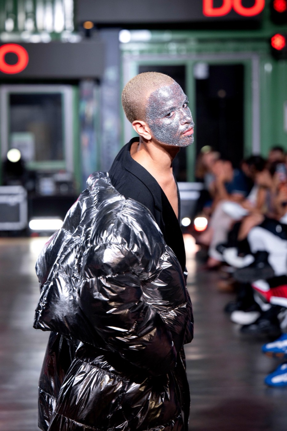 Performer walking a runway lit with red neon in front of an audience