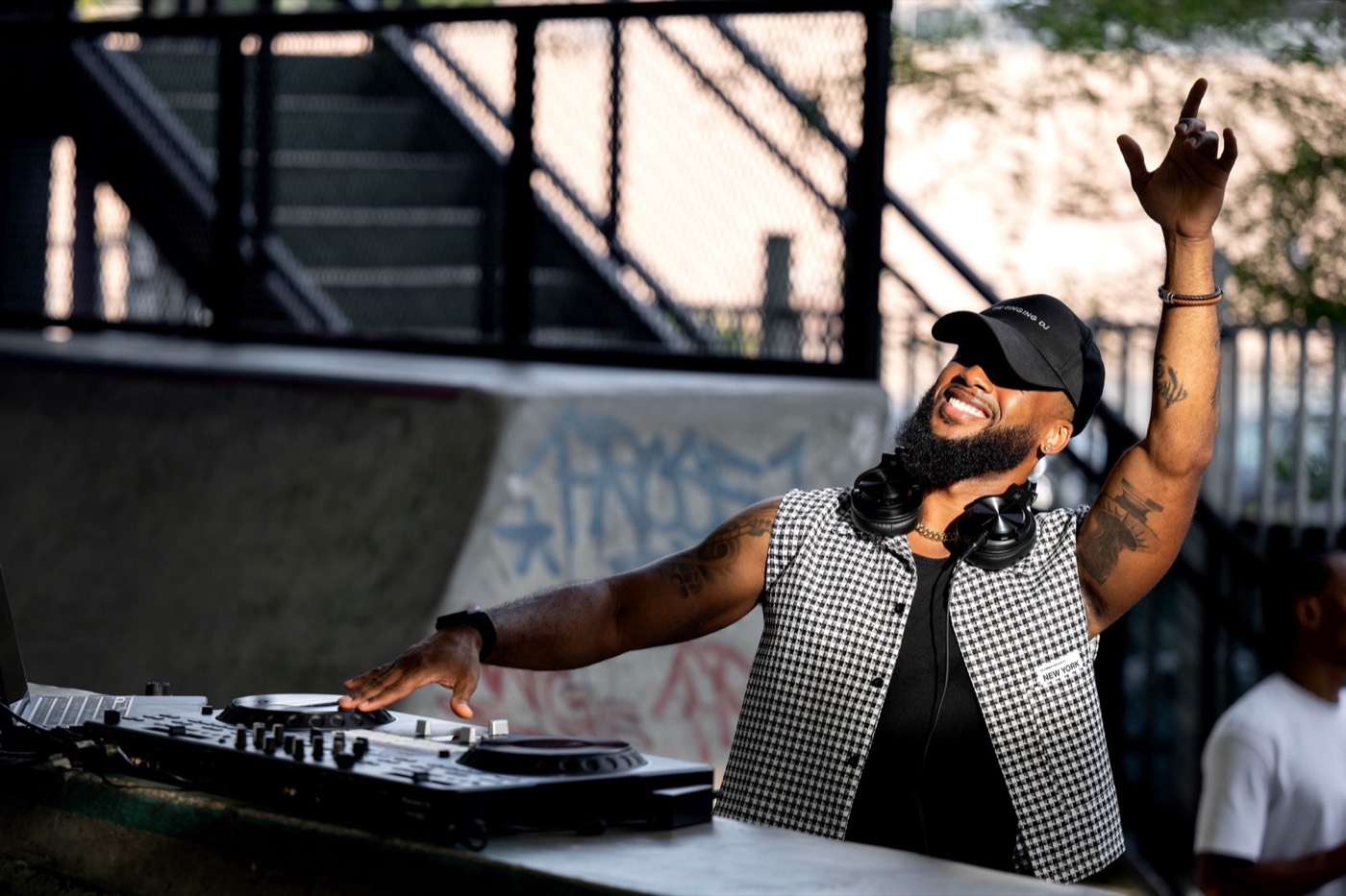 DJ raising an arm behind the decks under dark stage lighting