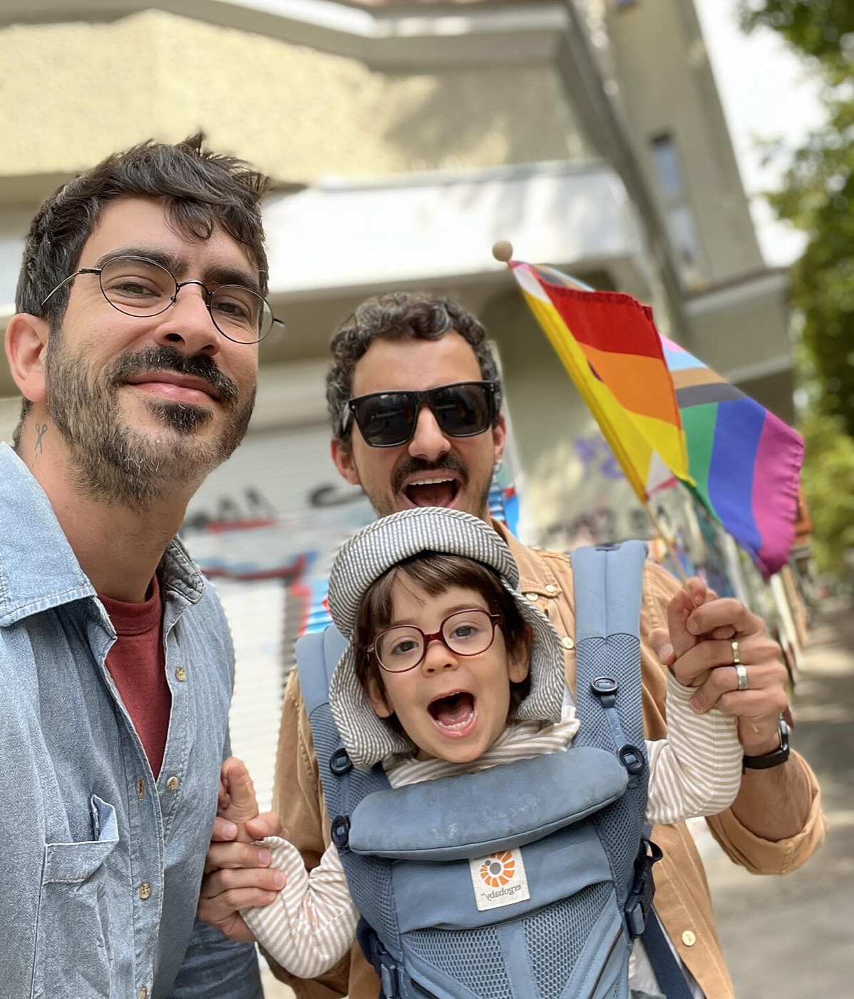 A family with a young child at a pride parade, rainbow flag in the background