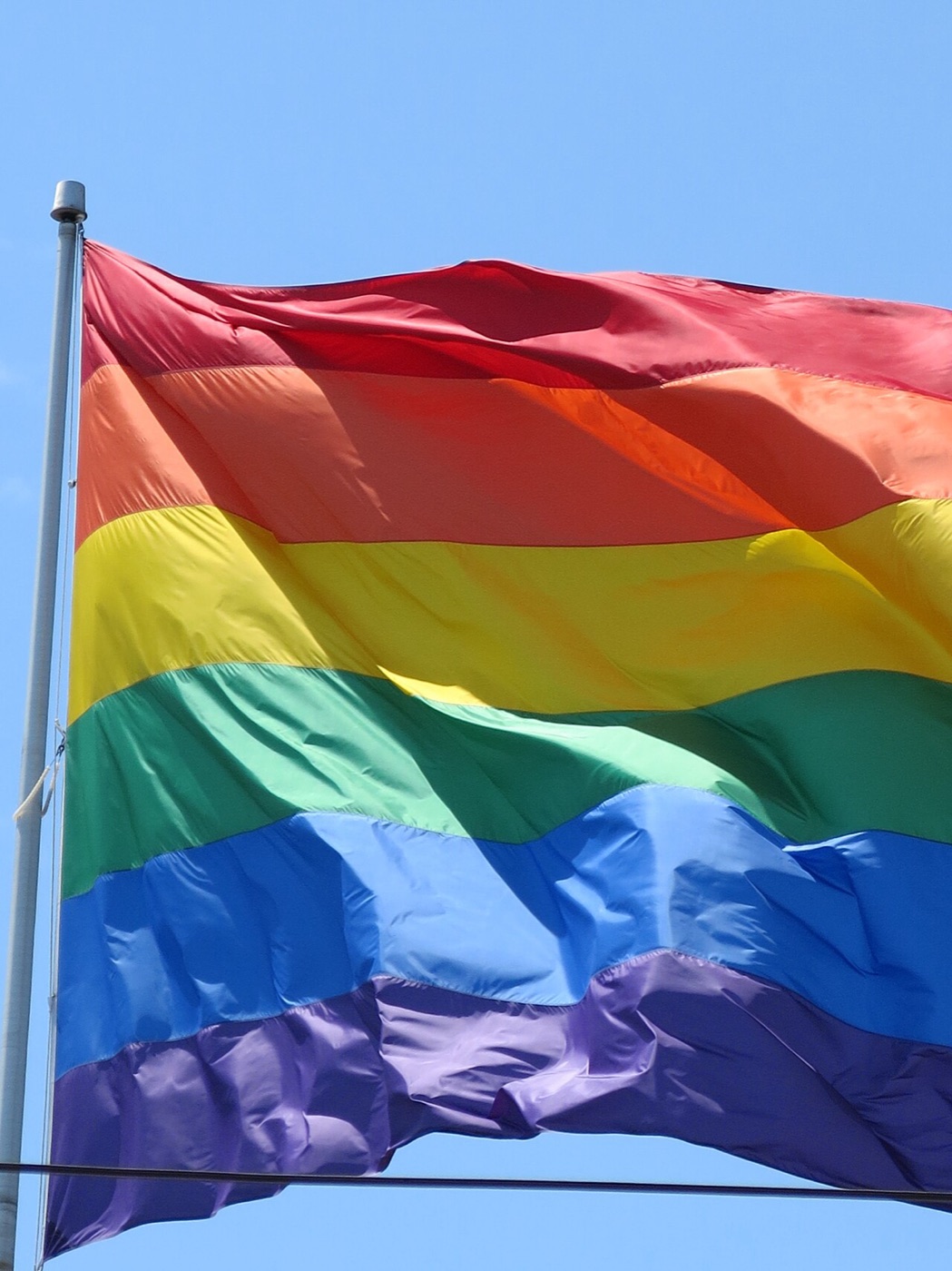 Pride rainbow flag waving against a blue sky